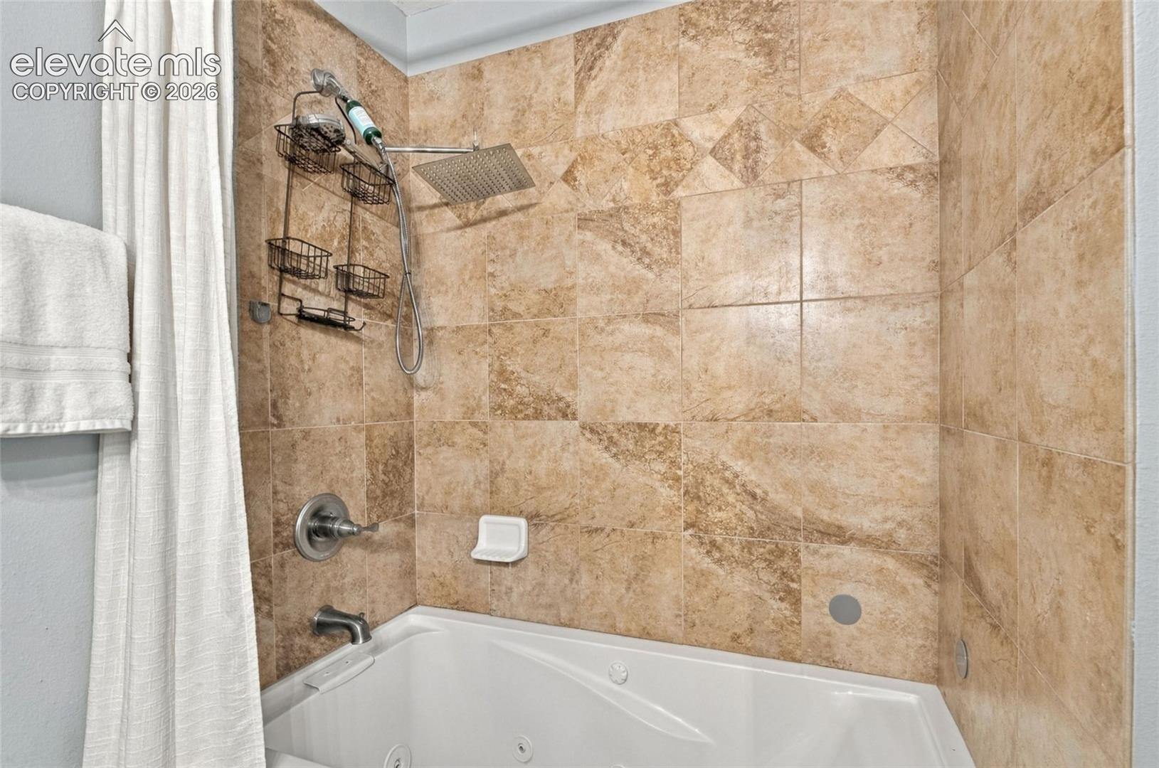 Jetted soaking tub with integrated shower surround, featuring square tile wall finish, rainfall shower head, and polished chrome fixtures
