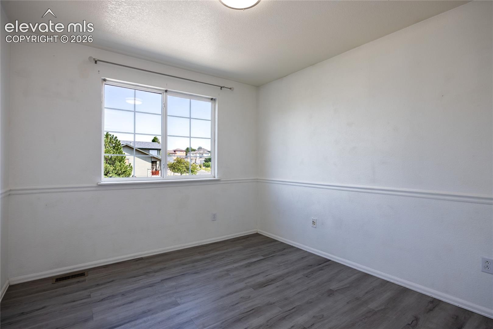 White walls with decorative chair rail, wood-finish flooring, and a multi-pane window