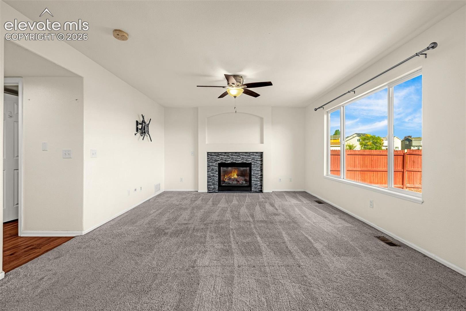 Living area featuring a fireplace with tiled surround and arched recessed niche, large picture windows, and a central ceiling fan