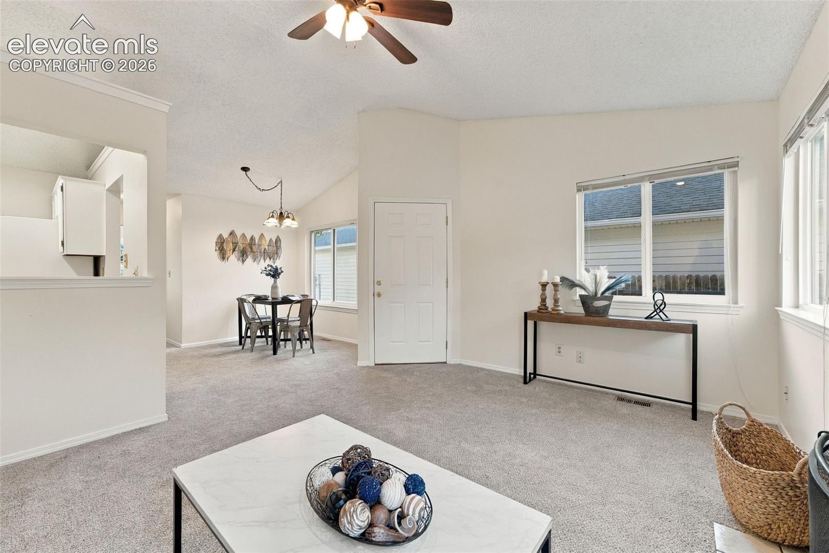 Vaulted ceilings, neutral wall tones, carpeted flooring, multi-pane windows, and a ceiling fan with integrated lighting