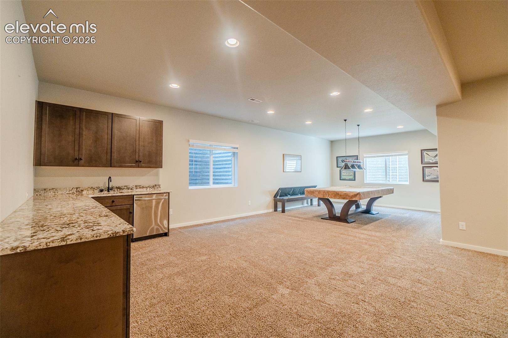 Entertainment room featuring recessed lighting, plush carpet flooring, a wet bar with a stainless steel sink and dishwasher, and two egress windows