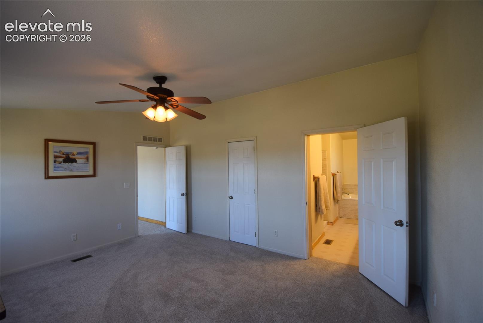 Neutral-toned carpeting, ceiling fan with integrated lighting, and a white six-panel door