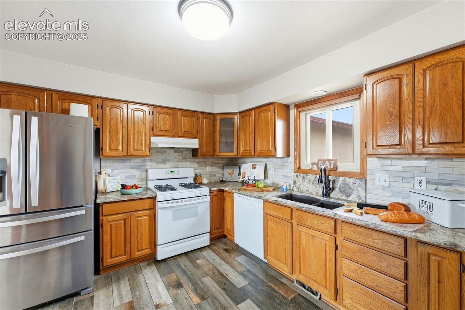 Kitchen featuring wood cabinetry, stainless steel refrigerator, white gas range, and wood-finish flooring