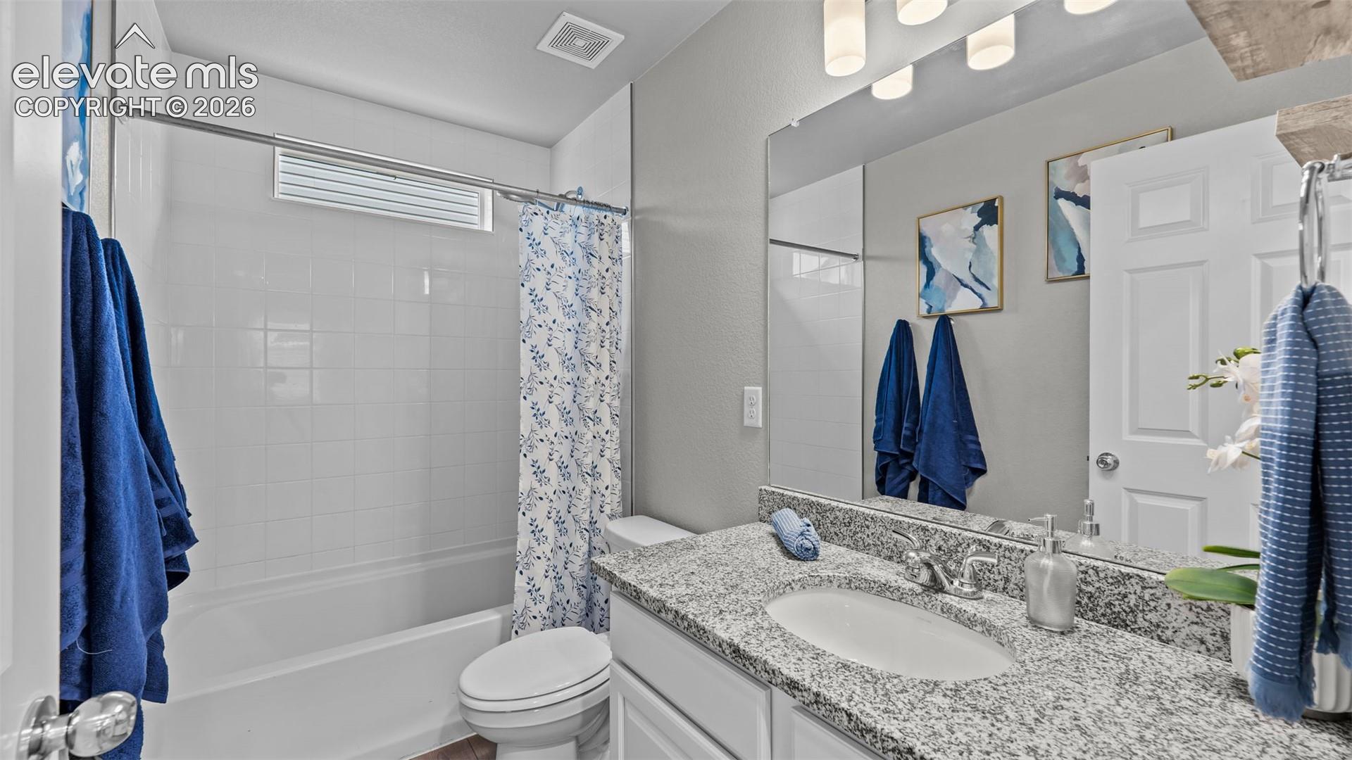 Bathroom featuring a stone-surface vanity with an integrated basin, a large wall-mounted mirror, overhead multi-light fixture, and a white porcelain tub-shower combination with tiled surround