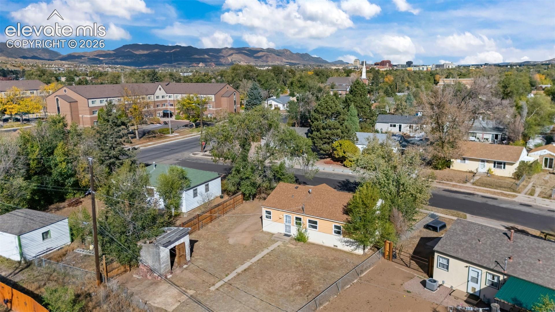 Aerial perspective of residential property featuring a pitched shingle roof, detached outbuilding, fenced perimeter, and mountain backdrop