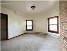 Interior space featuring an exposed brick accent wall, two large windows with dark wood trim, wall-to-wall carpeting, and a flush-mount ceiling light fixture