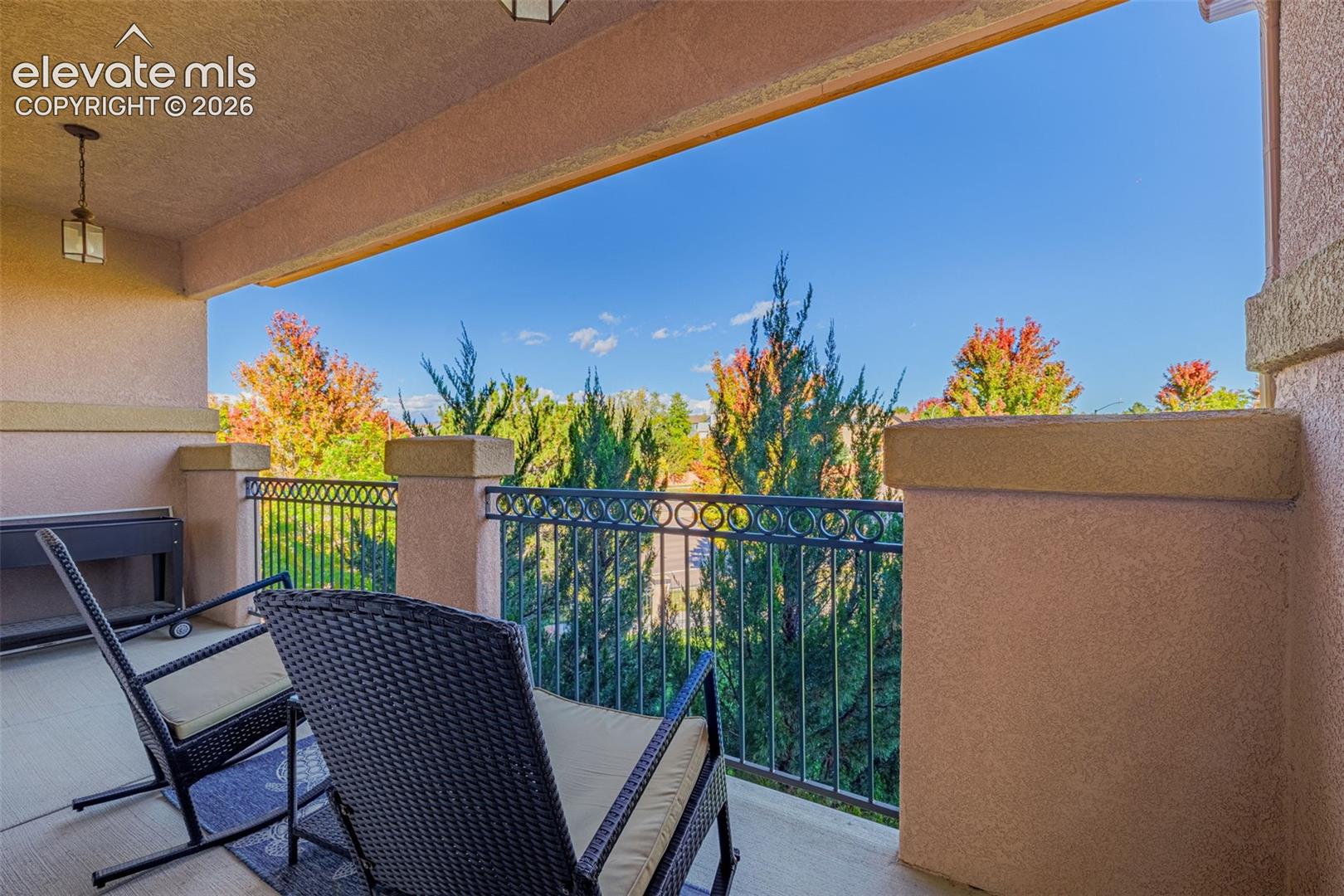 Covered balcony with stucco-finished pillars, decorative metal railing, and overhead lighting