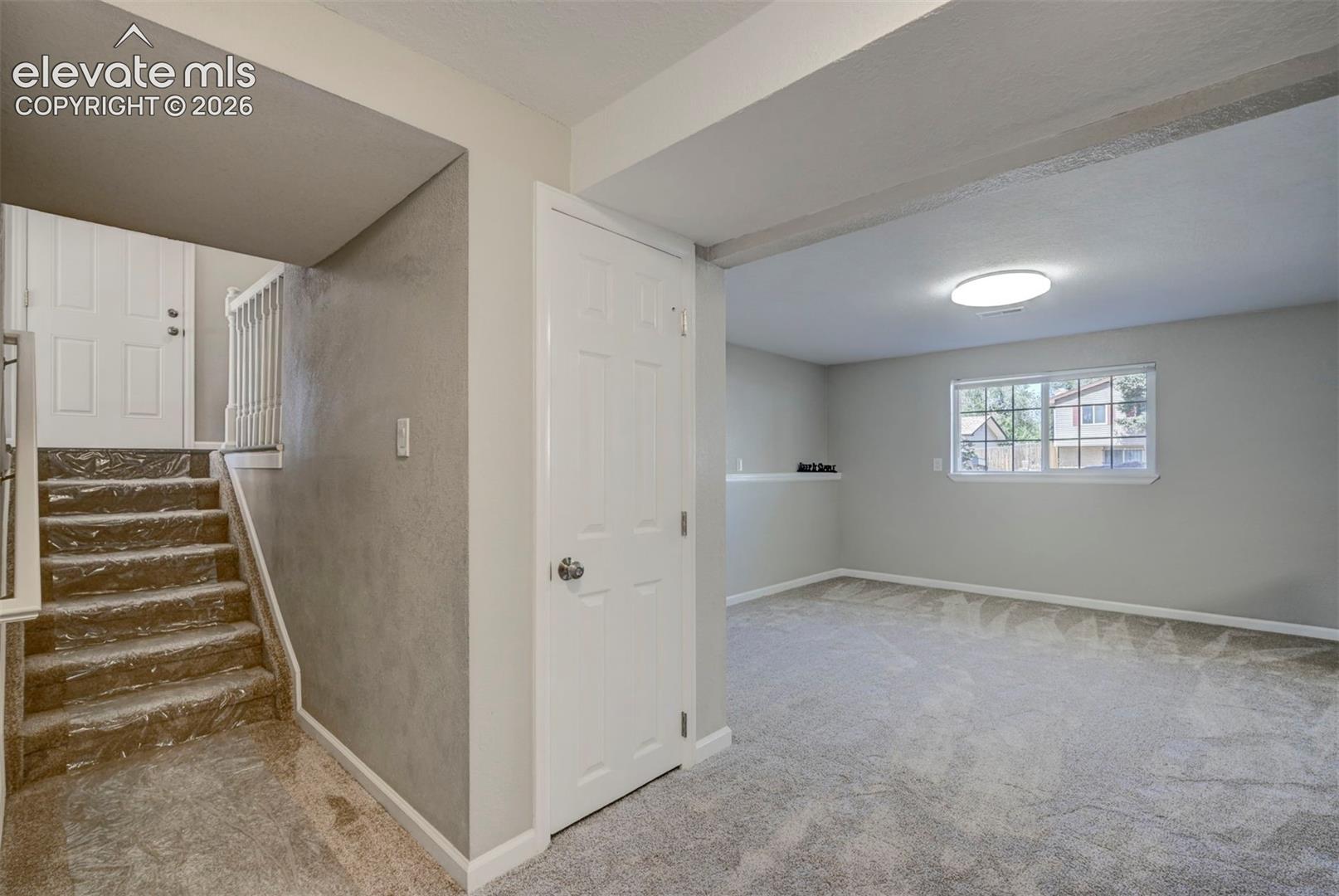 Interior space featuring wall-to-wall carpeting, neutral-toned walls, a white multi-panel interior door, and a flush-mount ceiling light fixture