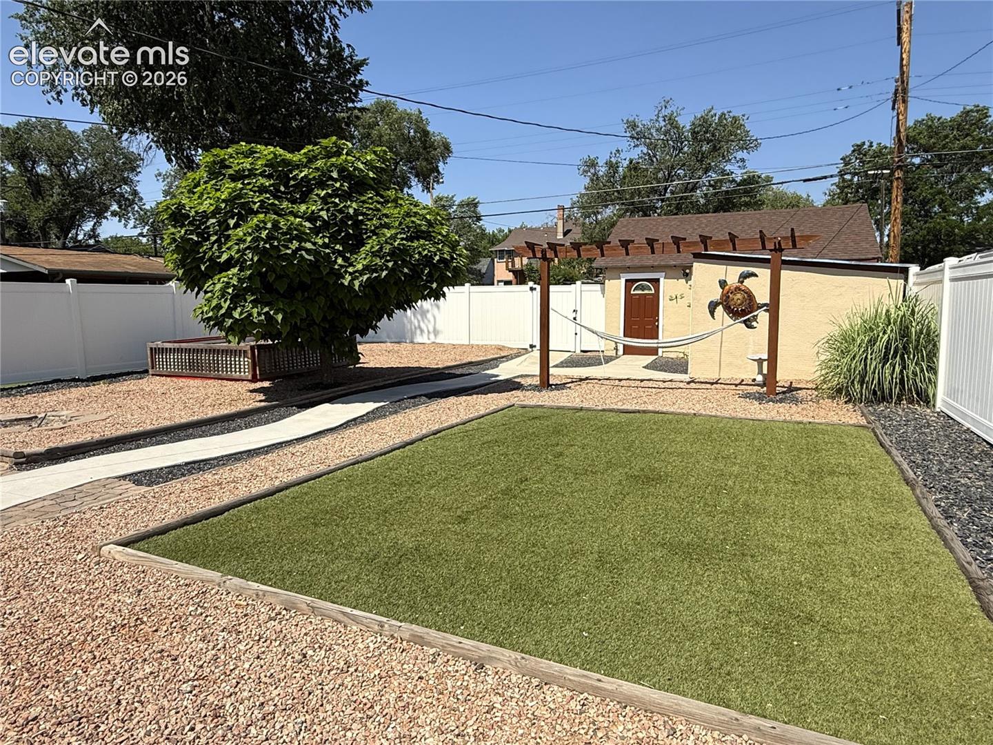 Fenced backyard featuring synthetic turf, decorative gravel ground cover, a wooden pergola, and a raised wooden planter