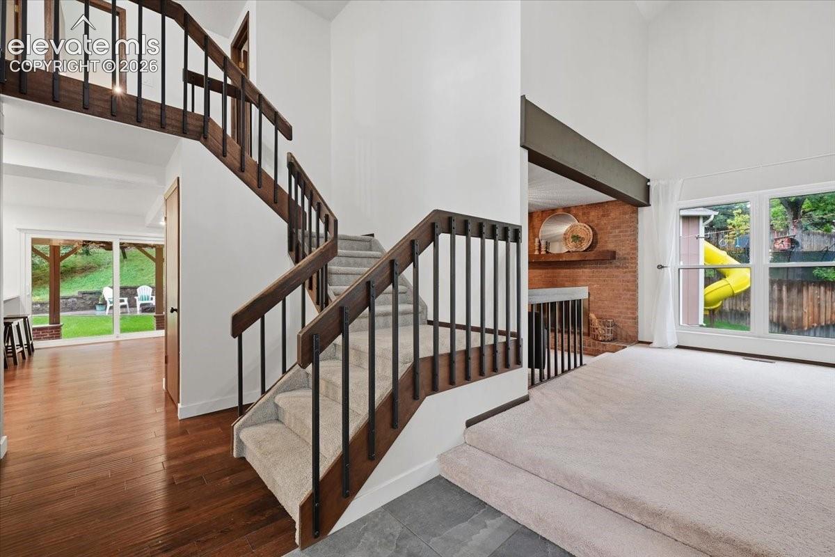 Hardwood flooring, carpeted stairs with Vaulted Entry, brick-clad interior wall, large windows, and a sliding glass door