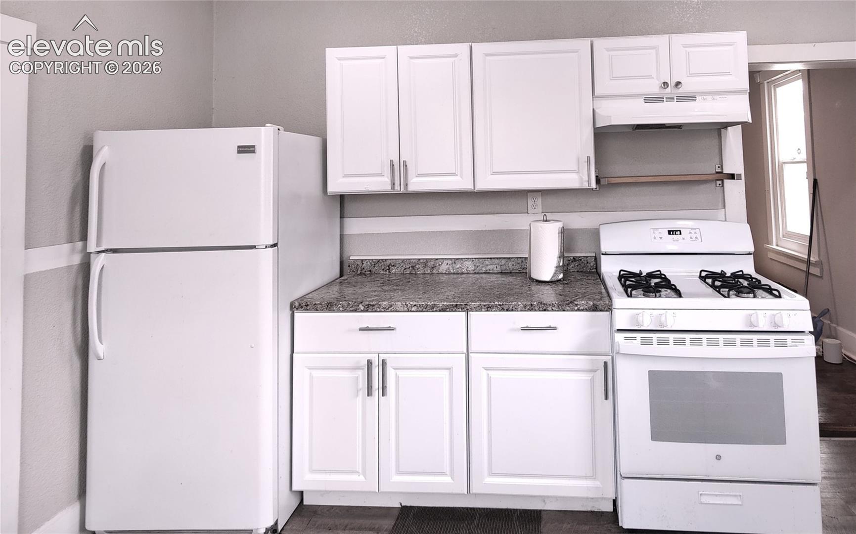 Full kitchen featuring a refrigerator, gas range, white cabinetry, and stone-look countertops