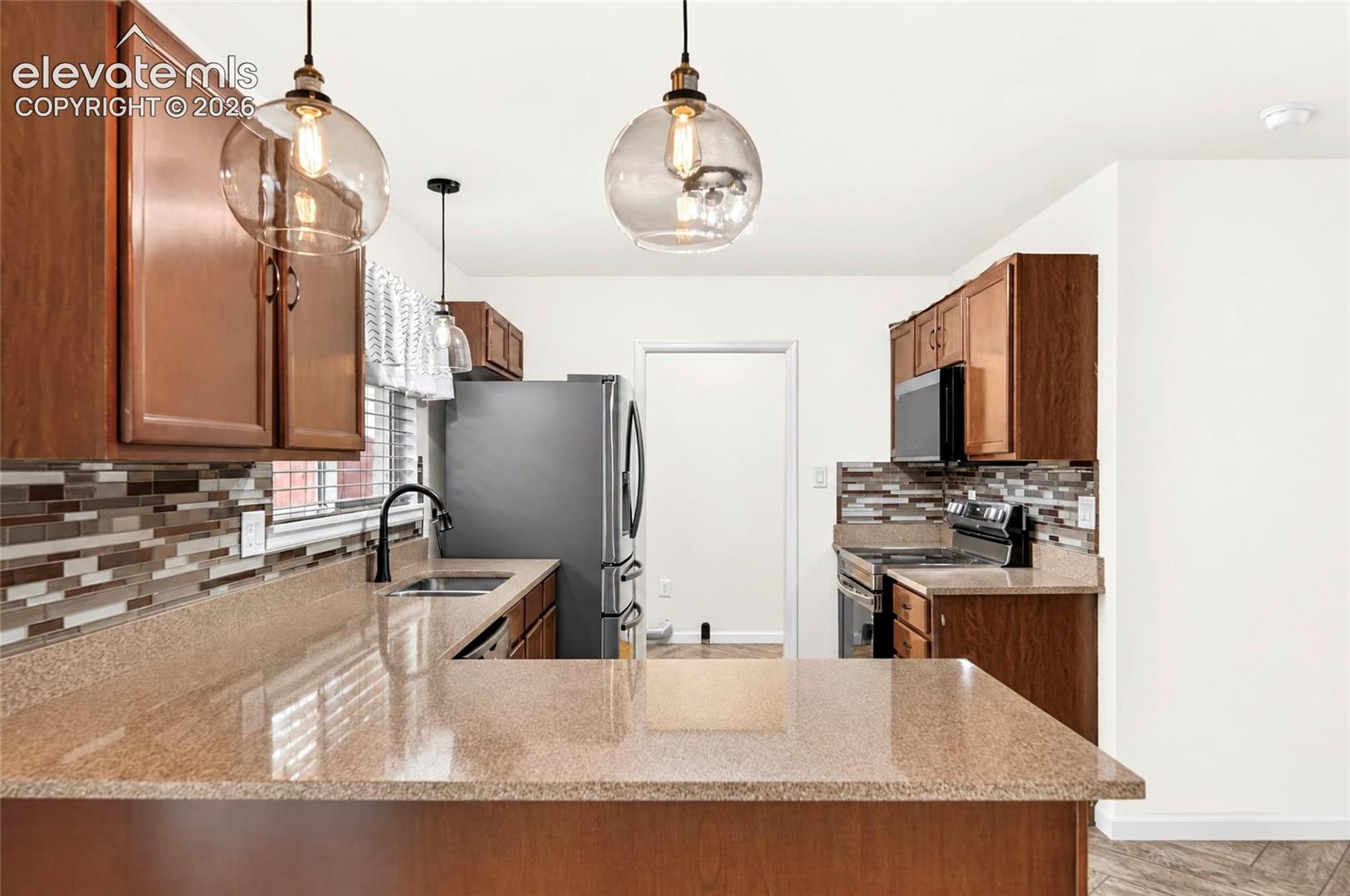 Kitchen featuring wood cabinetry, stone-finish countertops, decorative multi-tone tile backsplash, stainless steel appliances, and glass pendant lighting