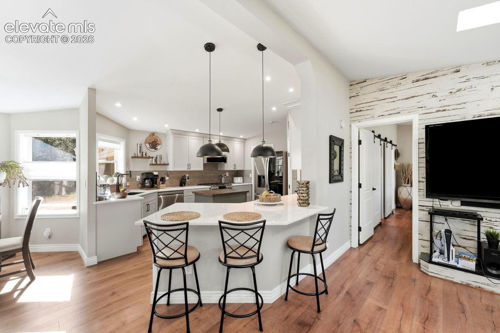 Wood-finish flooring throughout, kitchen with light-toned cabinetry and stainless steel appliances, breakfast bar with pendant lighting, and a white shiplap accent wall