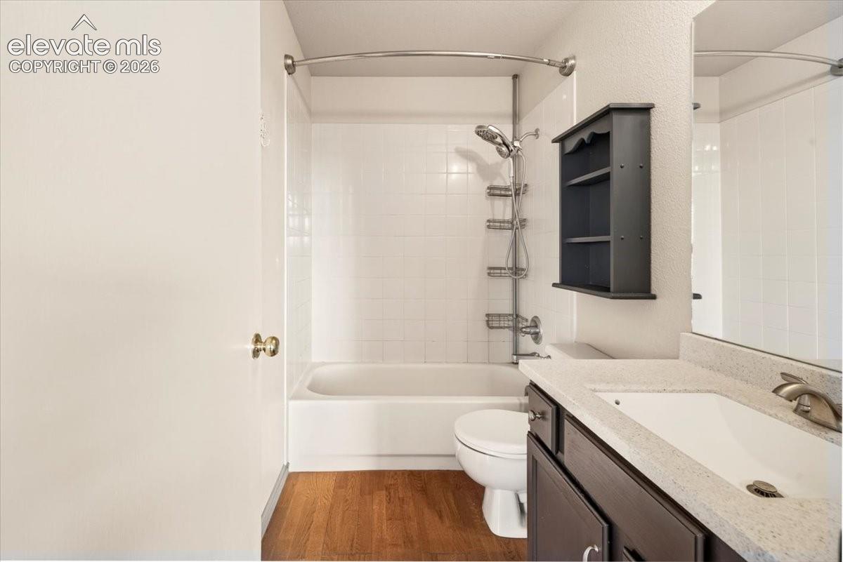 Bathroom on main level featuring wood-finish flooring, a vanity with a light-toned solid surface countertop, an integrated sink, and a shower-tub combination with white tile surround