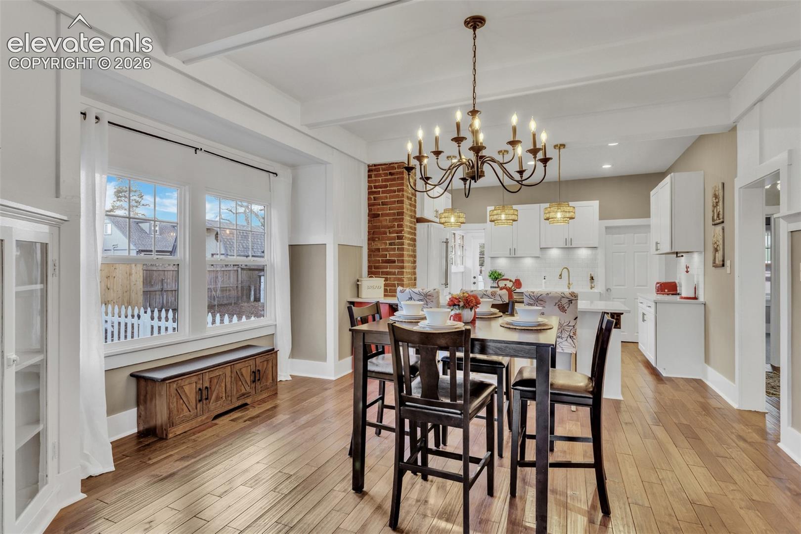 Dining area featuring a prominent chandelier, wood-finish flooring, exposed brick detailing, and white coffered ceilings
