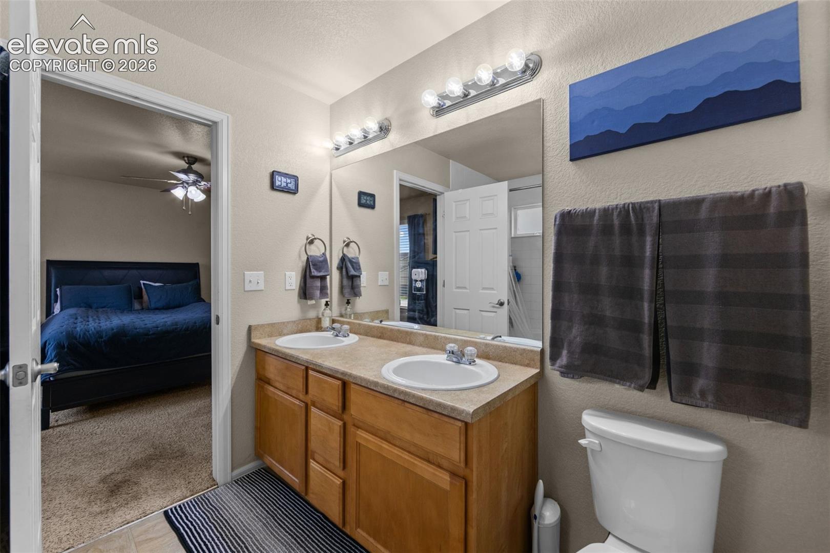 Bathroom featuring a double vanity with integrated sinks, wood-finish cabinetry, a wall-mounted mirror, and overhead strip lighting