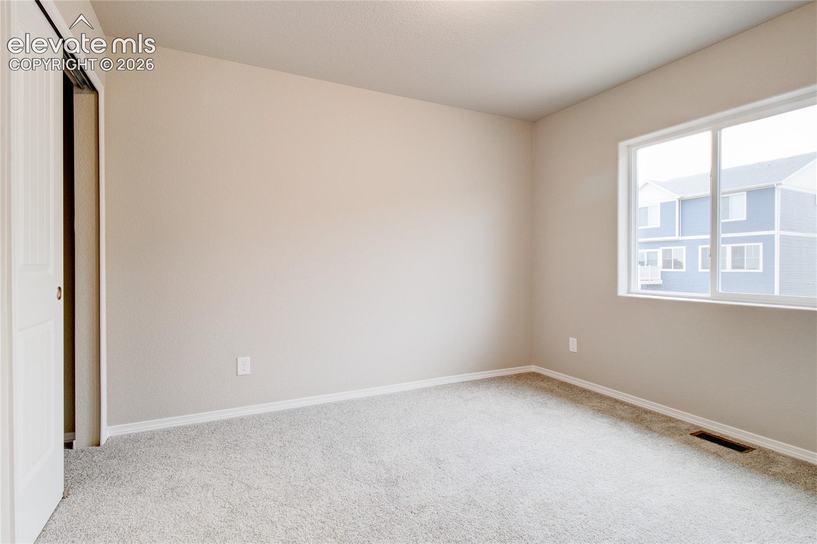 Neutral-toned interior space featuring wall-to-wall carpeting, a large sliding window, and a built-in closet with sliding panel doors