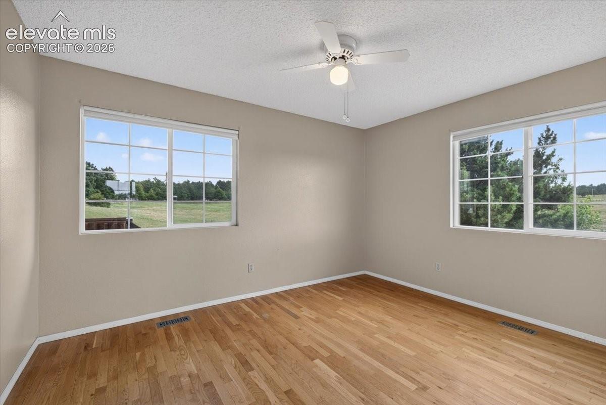 Main level bedroom with Wood-finish flooring, dual windows with grid detailing, and a ceiling-mounted light fixture with fan