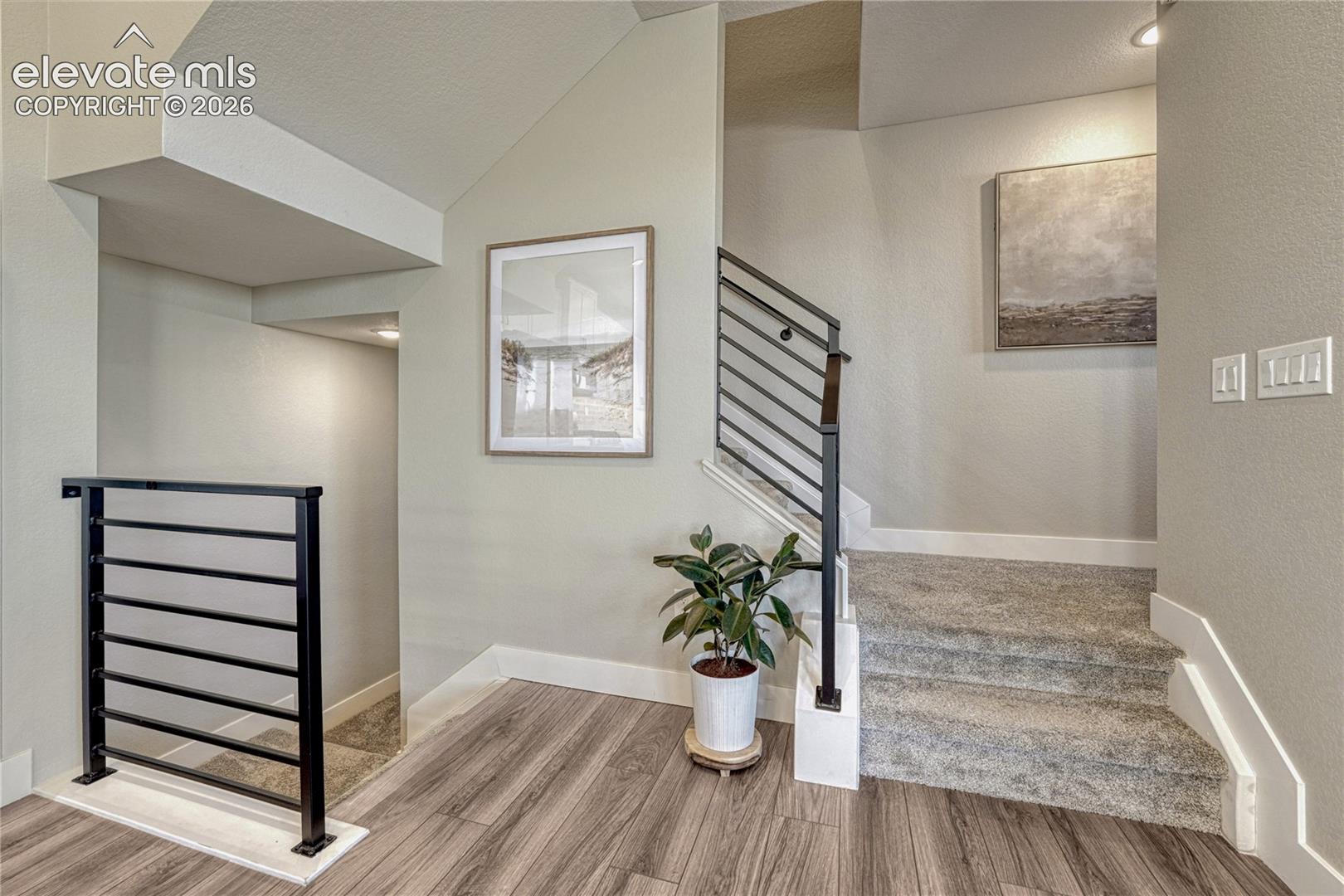 Entry featuring wood-finish flooring, staircase with carpeted treads, and matte black horizontal railing