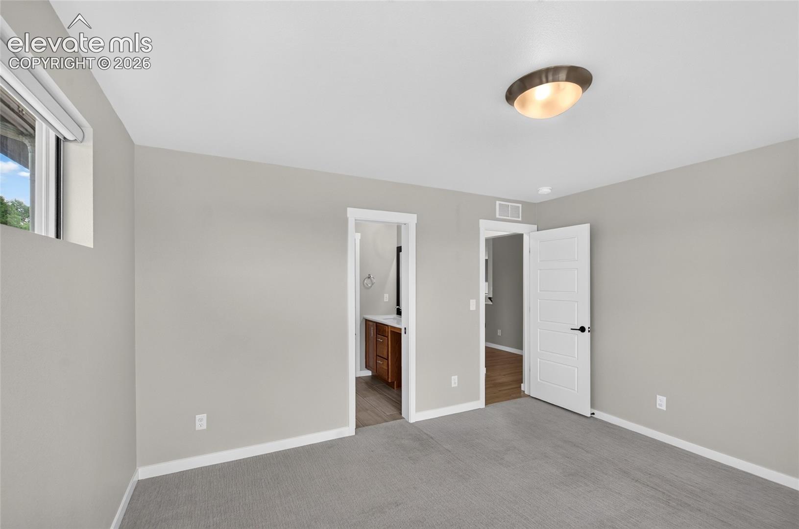 Main floor bedroom with bath access Carpeted bedroom featuring light gray walls, a flush-mount ceiling light fixture, and white trim