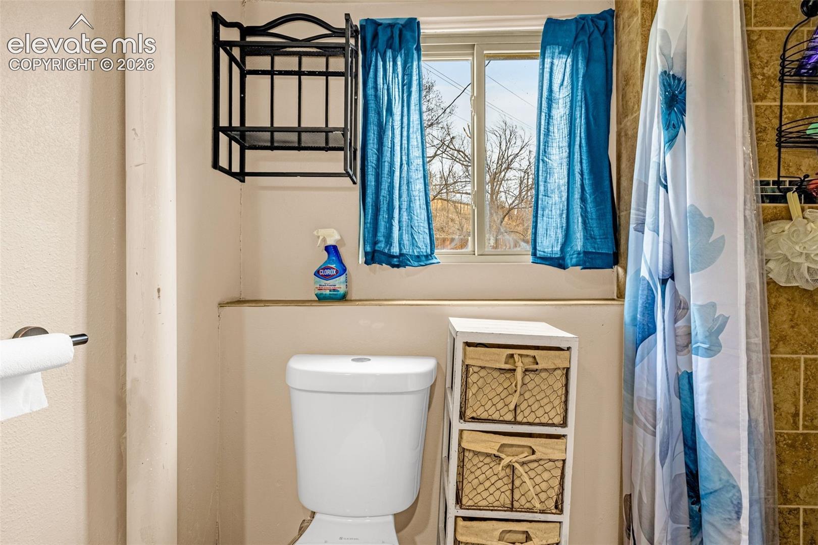Bathroom featuring a sliding window, a dual-flush toilet, and wall-mounted metal shelving
