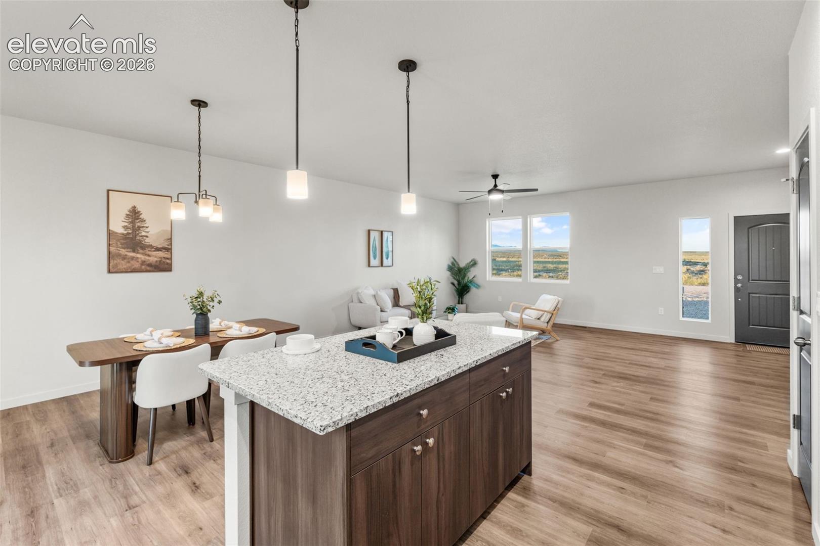 Kitchen island with a stone countertop and dark-finish cabinetry, wood-finish flooring, dual hanging pendant lights, and a ceiling fan
