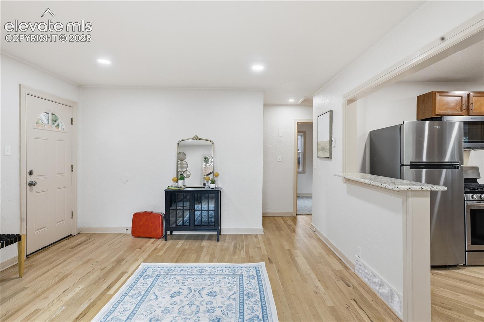 Interior space featuring wood-finish flooring, recessed lighting, and a kitchen pass-through with stone-finish countertop