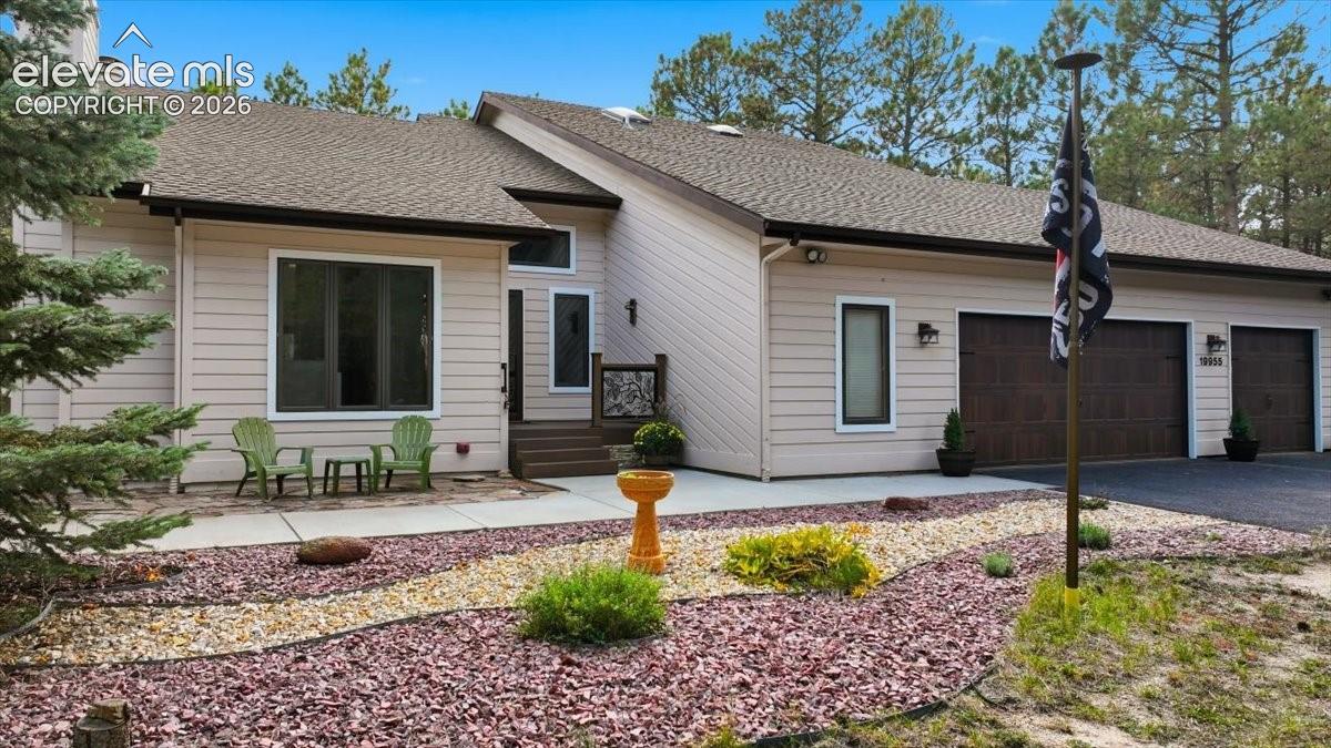 Siding exterior with a multi-car garage, pitched shingle roof, and a landscaped front yard with decorative rock and shrubbery