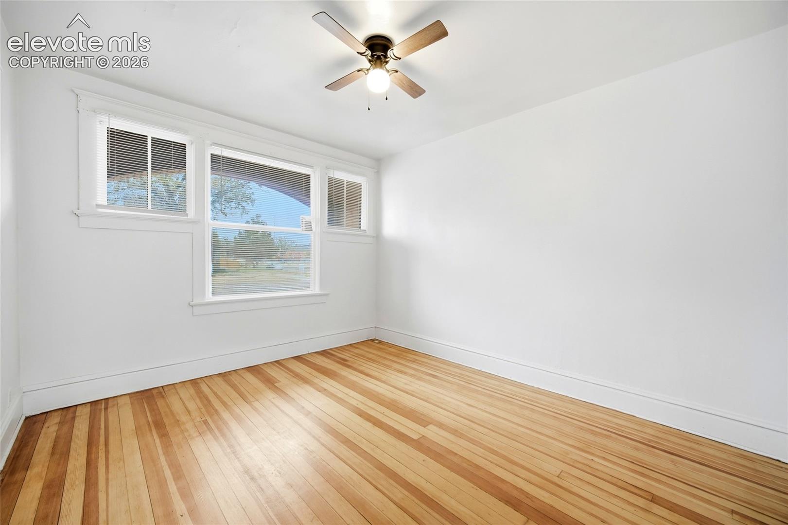 Room featuring wood-finish flooring, a multi-pane window configuration, and a ceiling-mounted light fixture with integrated fan