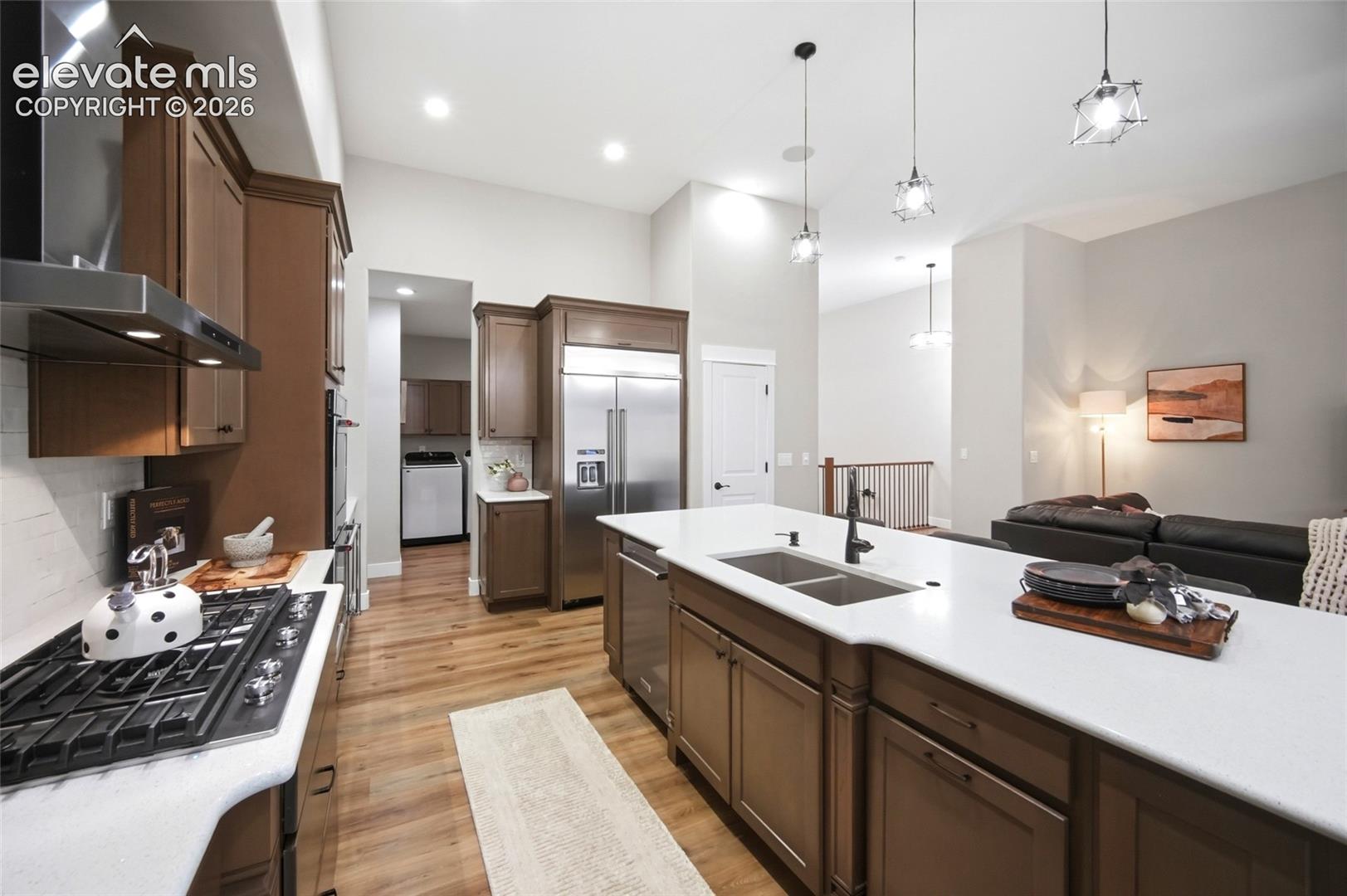 Kitchen featuring dark wood-finish cabinetry, a large center island with a quartz countertop, stainless steel appliances, a built-in gas cooktop, and recessed and pendant lighting