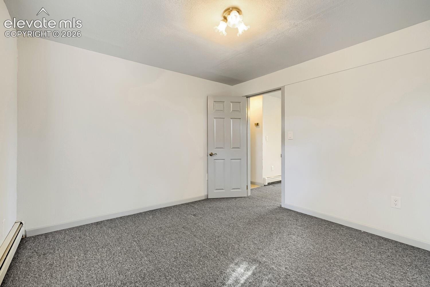 Neutral wall paint, textured ceiling, gray carpet flooring, white paneled door, flush mount ceiling light