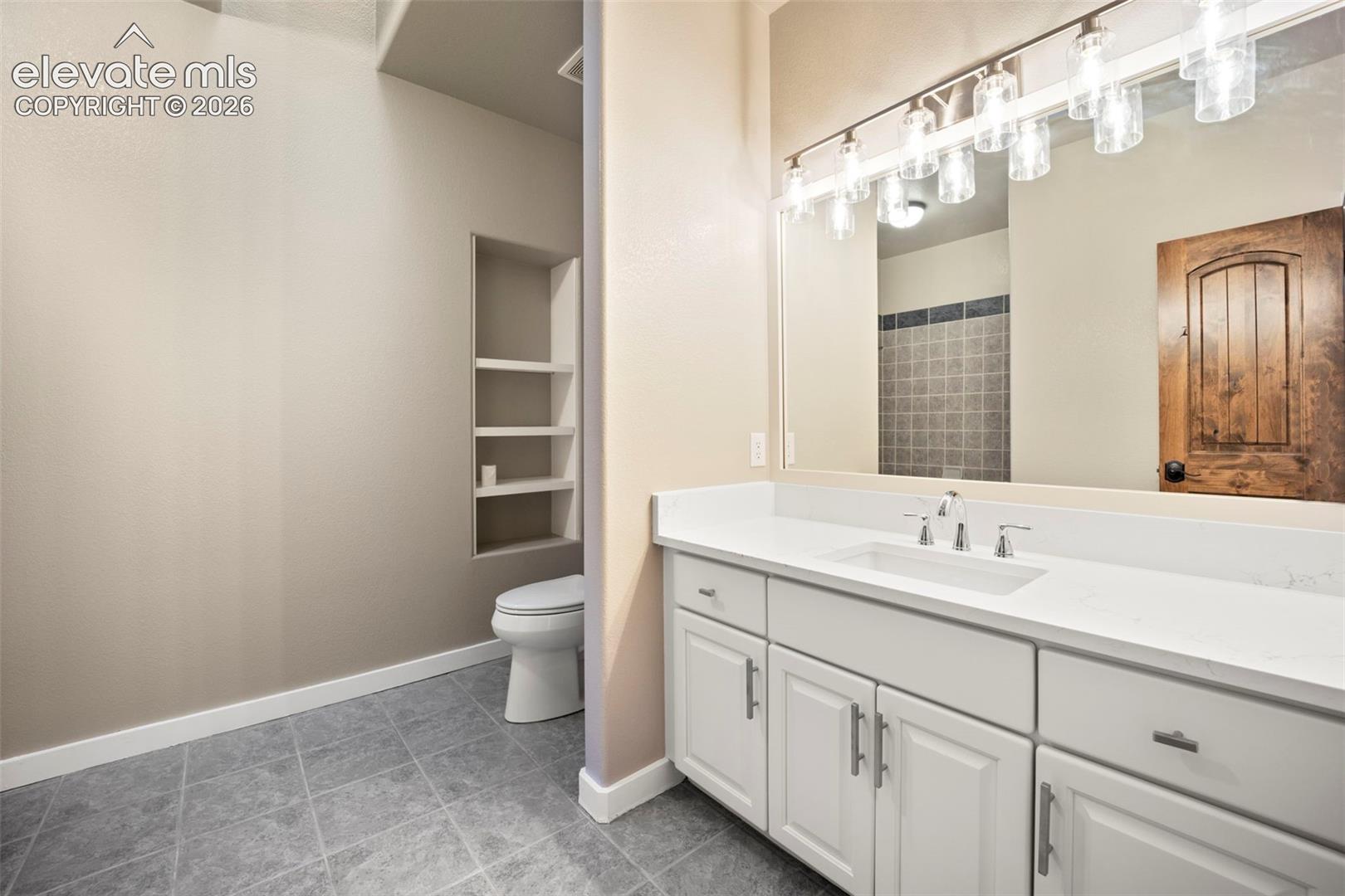 Bathroom featuring a spacious vanity with an integrated sink, white cabinetry, and a large mirror with contemporary lighting