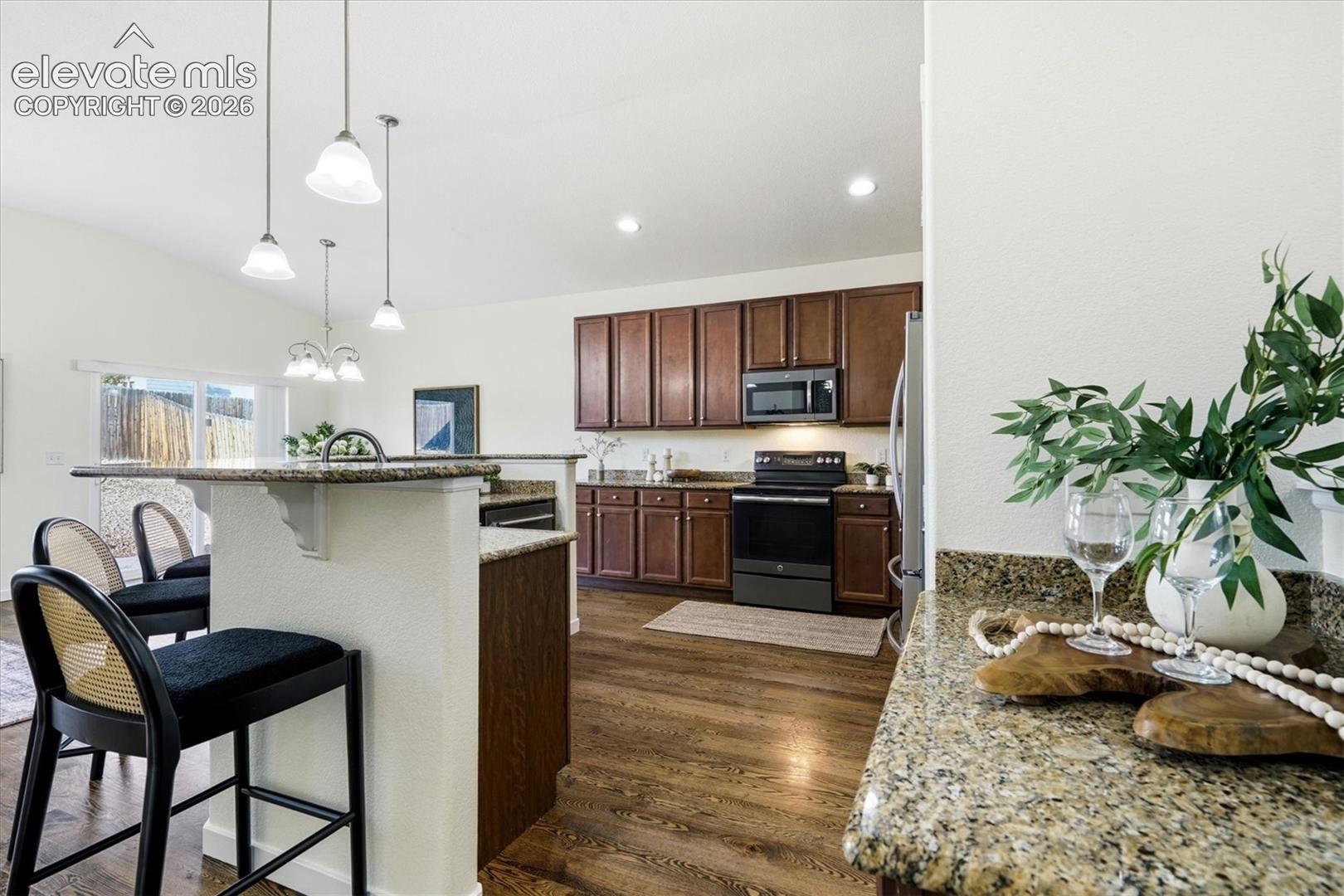 Kitchen featuring wood-finish flooring, dark wood cabinetry, granite countertops, and stainless steel appliances