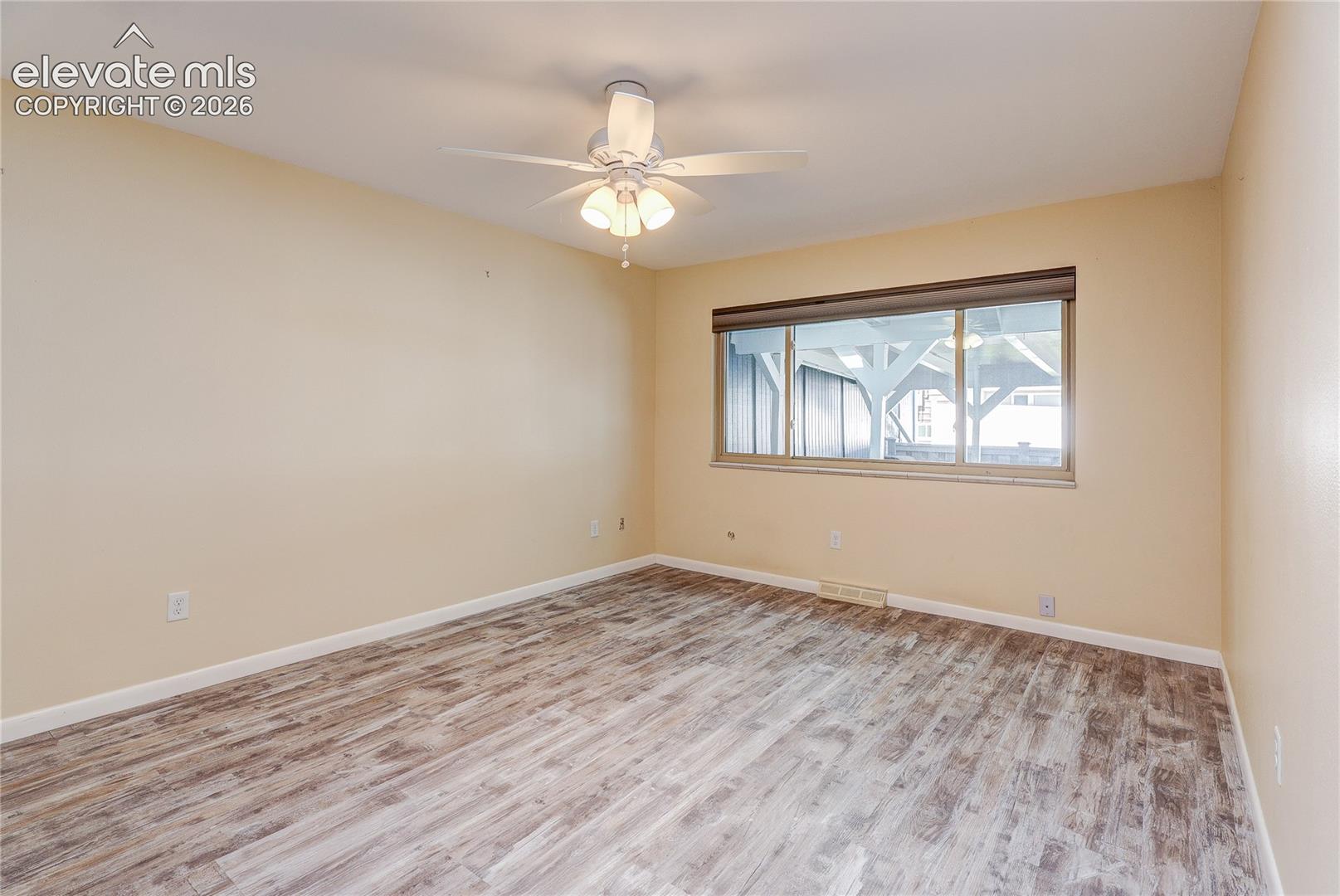 Room featuring wood-finish flooring, a neutral color palette, a ceiling fan with integrated lighting, and a large horizontal window