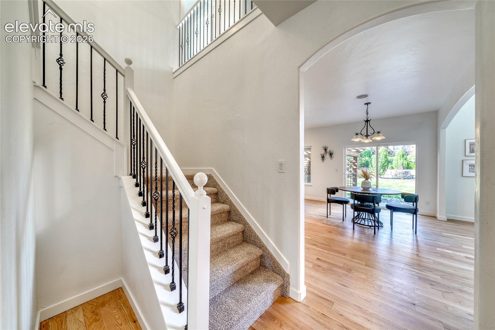 Carpeted staircase with wrought iron balusters, arched entryway, hard surface flooring, and a dining area with a chandelier
