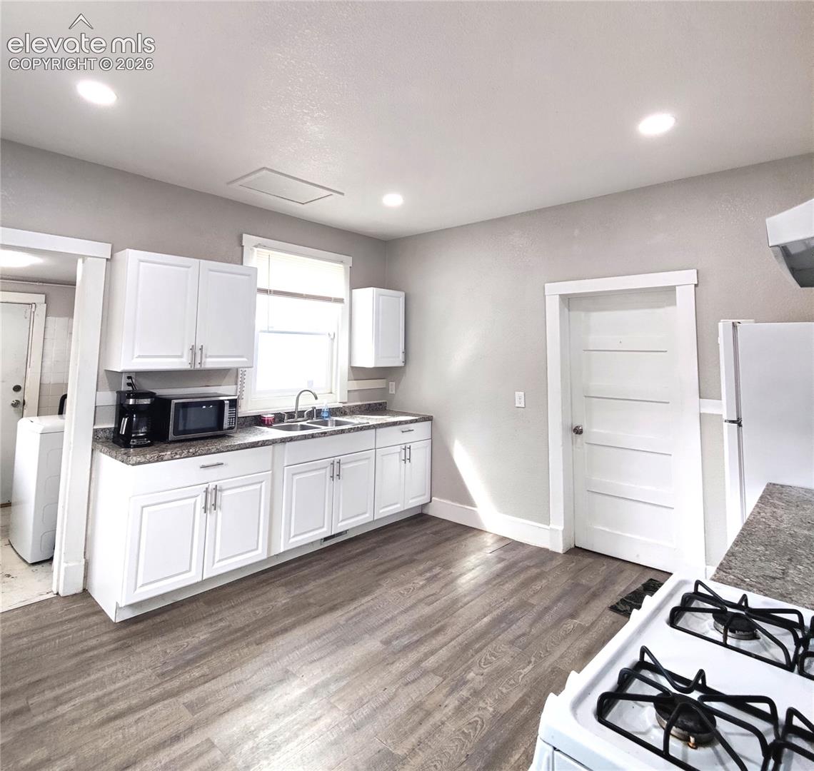 Kitchen featuring wood-finish flooring, white cabinetry, a double basin sink, and recessed ceiling lighting