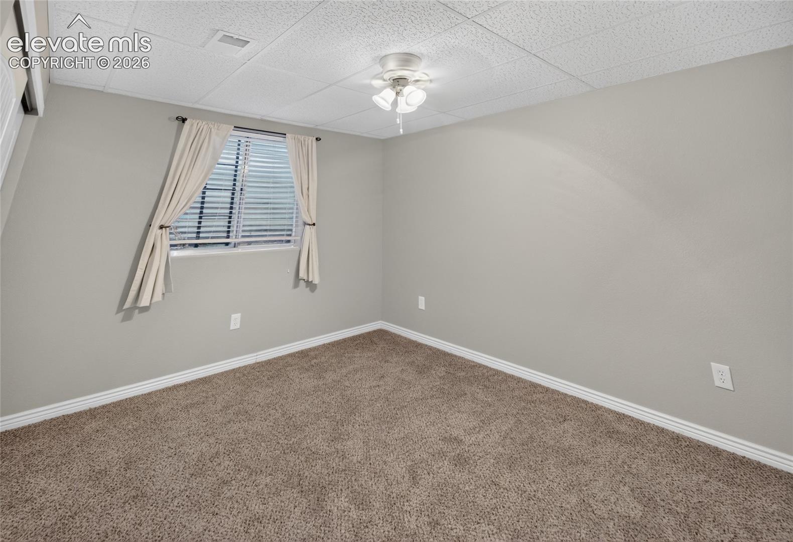 Neutral wall palette, wall-to-wall carpeting, drop ceiling, and a ceiling-mounted light fixture with a fan