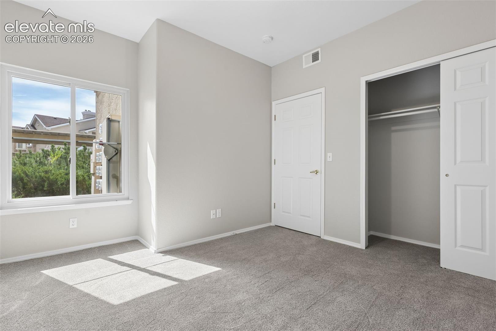 Light gray carpeting, white trim, white sliding closet door, white raised panel door, and a white framed window