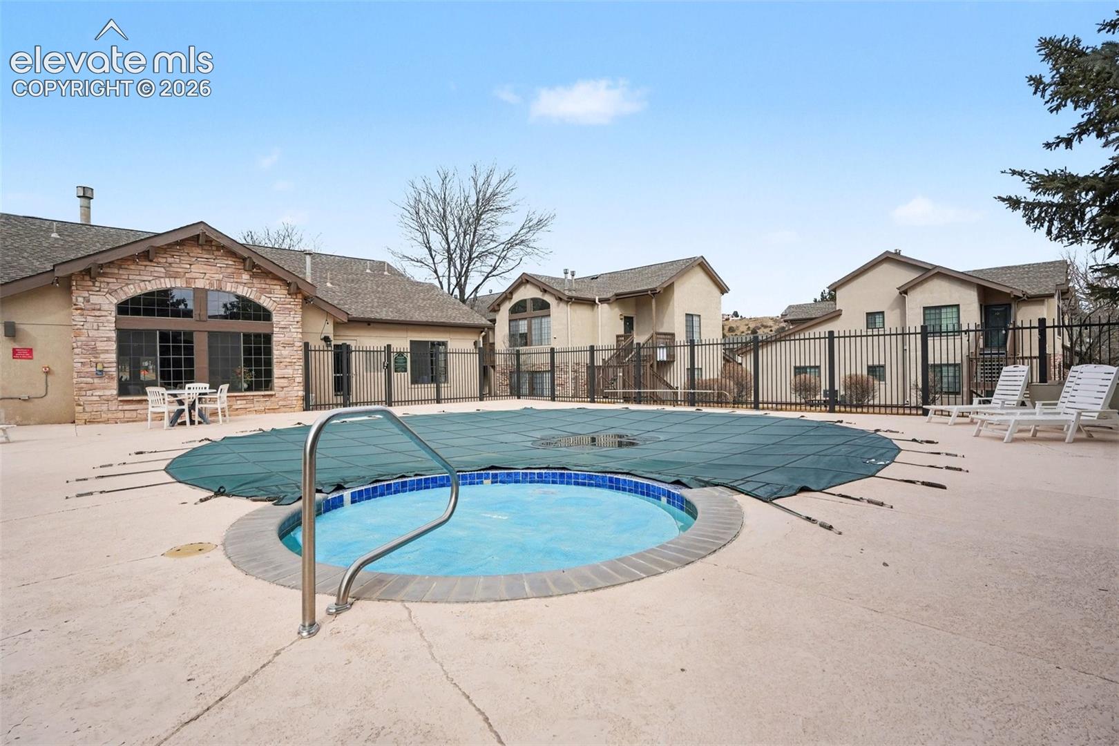 Community swimming pool featuring a concrete deck, circular hot tub with tile surround, and perimeter metal fencing