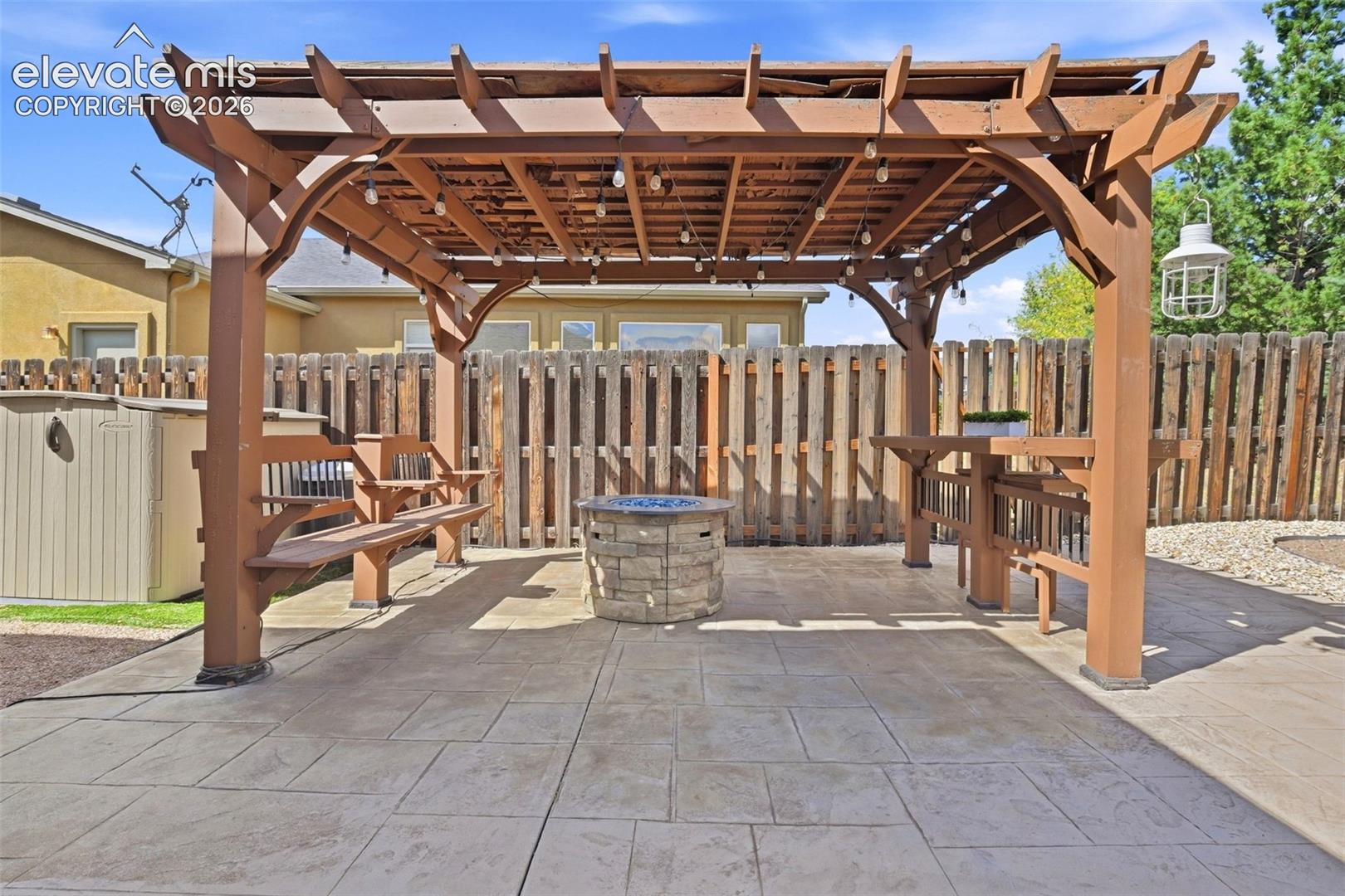 Stamped concrete patio with a stone clad firepit and anchored pergola featuring built-in seating and tabletop area.