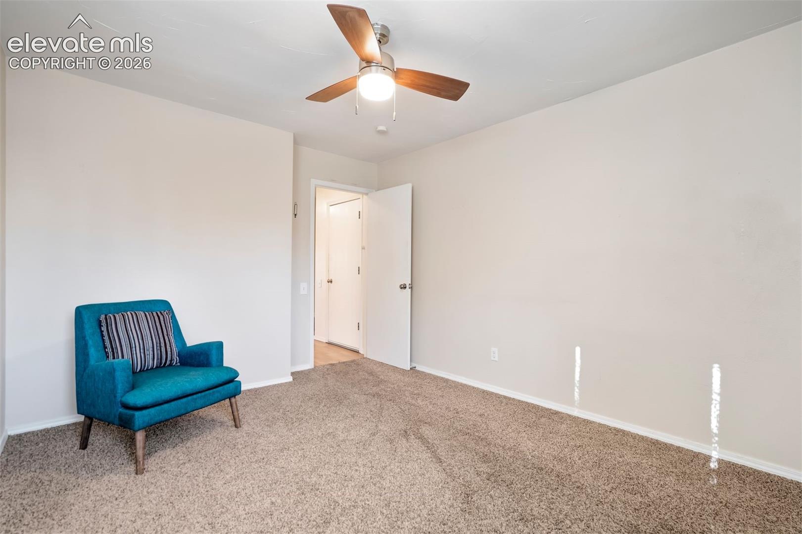 Neutral-toned interior space featuring carpeting, a three-blade ceiling fan with integrated lighting, and a hollow-core door