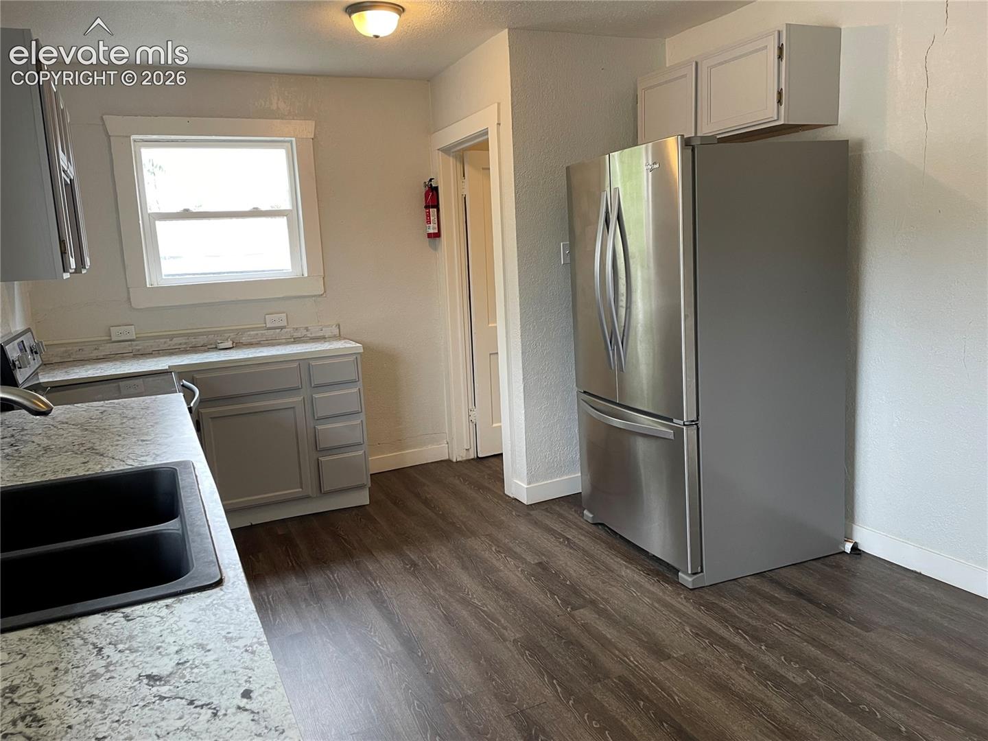 Kitchen featuring wood-finish flooring, light grey cabinetry, a stainless steel refrigerator, and speckled countertops