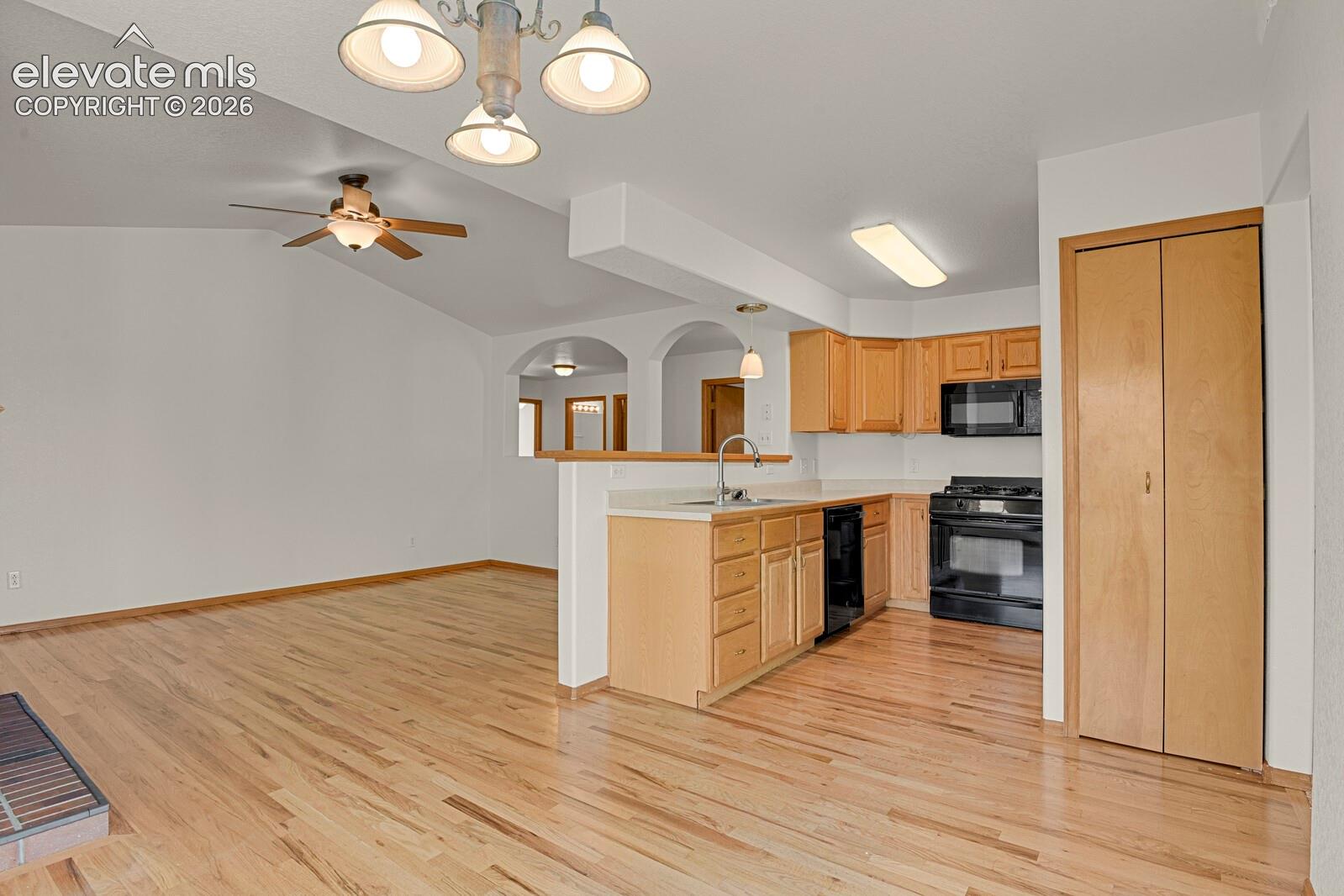 Vaulted ceilings, wood-finish flooring, kitchen with black appliances, light wood cabinetry, and a ceiling fan