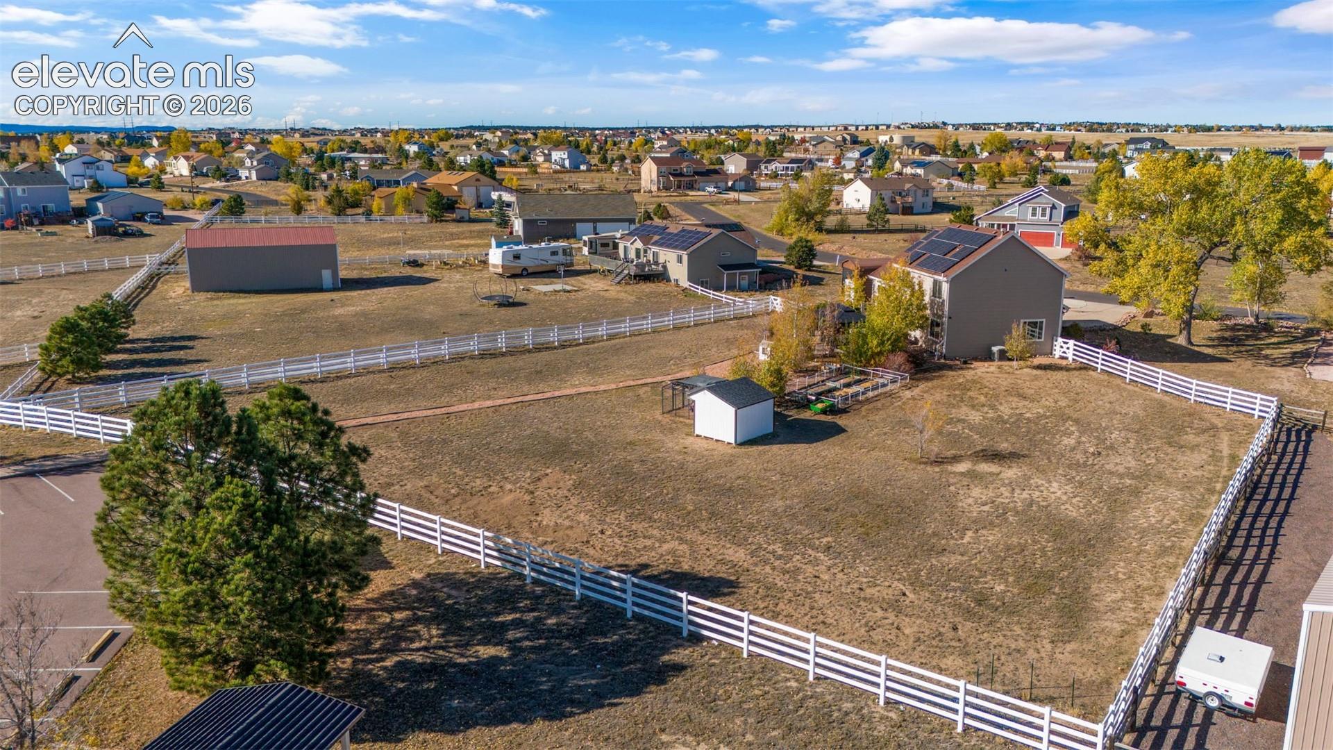 Extensive lot featuring a white perimeter fence, solar roof panels, detached storage building, and mature tree landscaping