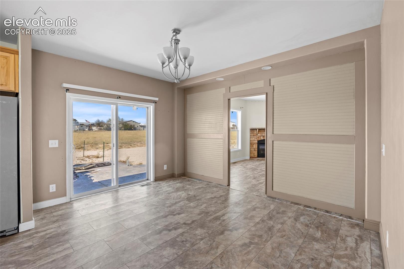 Dining area featuring tile flooring, sliding glass door, decorative wall paneling, and a tiered chandelier