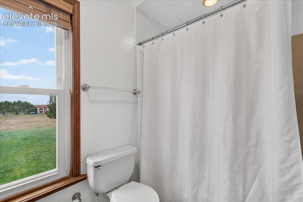 Full bathroom featuring a window with wood trim, white toilet, and chrome hardware