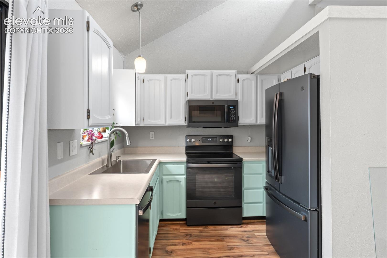 U-shaped kitchen featuring white upper cabinetry, mint green lower cabinetry, wood-finish flooring, a stainless steel sink, and dark-finish appliances