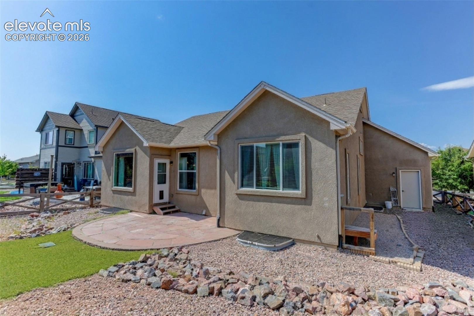 Stucco exterior with multiple windows, a stone patio, and a gravel landscape