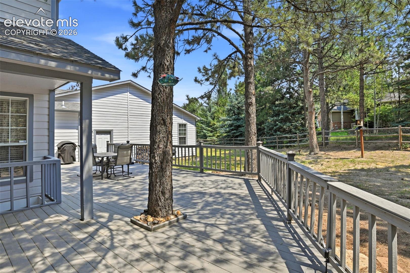Expansive outdoor deck with a continuous railing system, featuring mature trees and a fenced property boundary