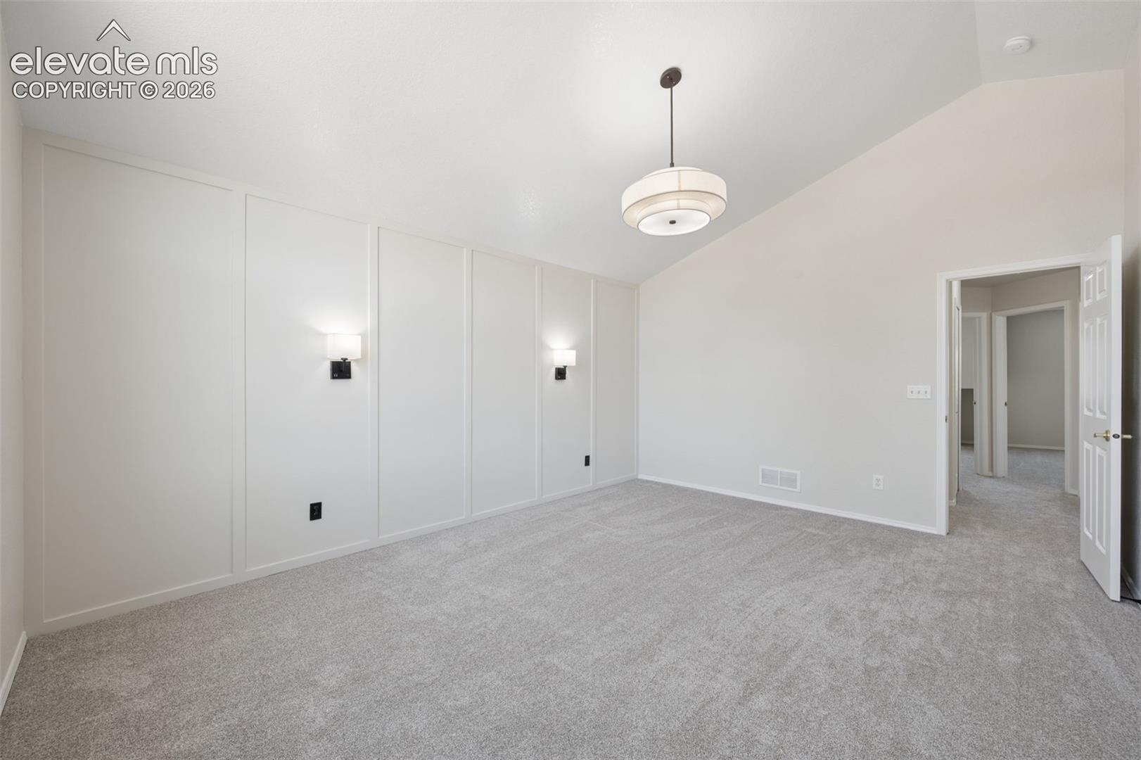 Vaulted ceilings, board and batten wall detailing, dual wall-mounted light fixtures, pendant chandelier, and neutral wall-to-wall carpeting